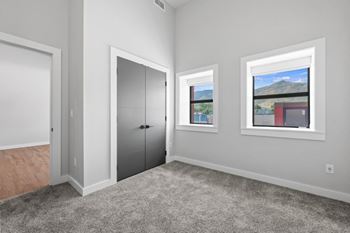 A room with a grey carpet, a white door, a grey wardrobe and a window with a view of the mountains.